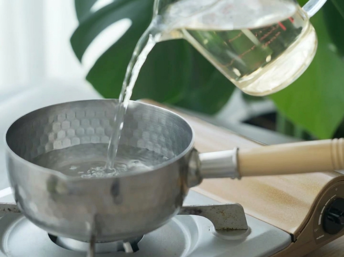 Klare Dashi-Brühe wird aus einem Messbecher in einen kleinen Edelstahltopf gegossen.