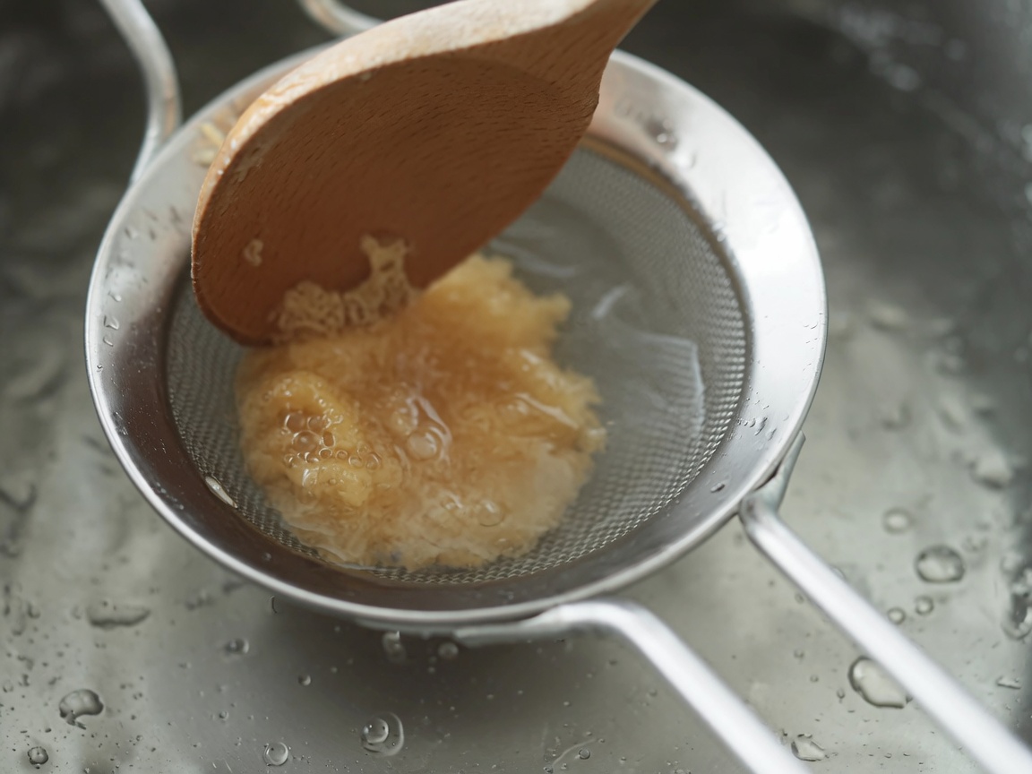 Weiße Miso-Paste wird mit einem Holzlöffel durch ein Metallsieb in die kochende Suppe gerührt.