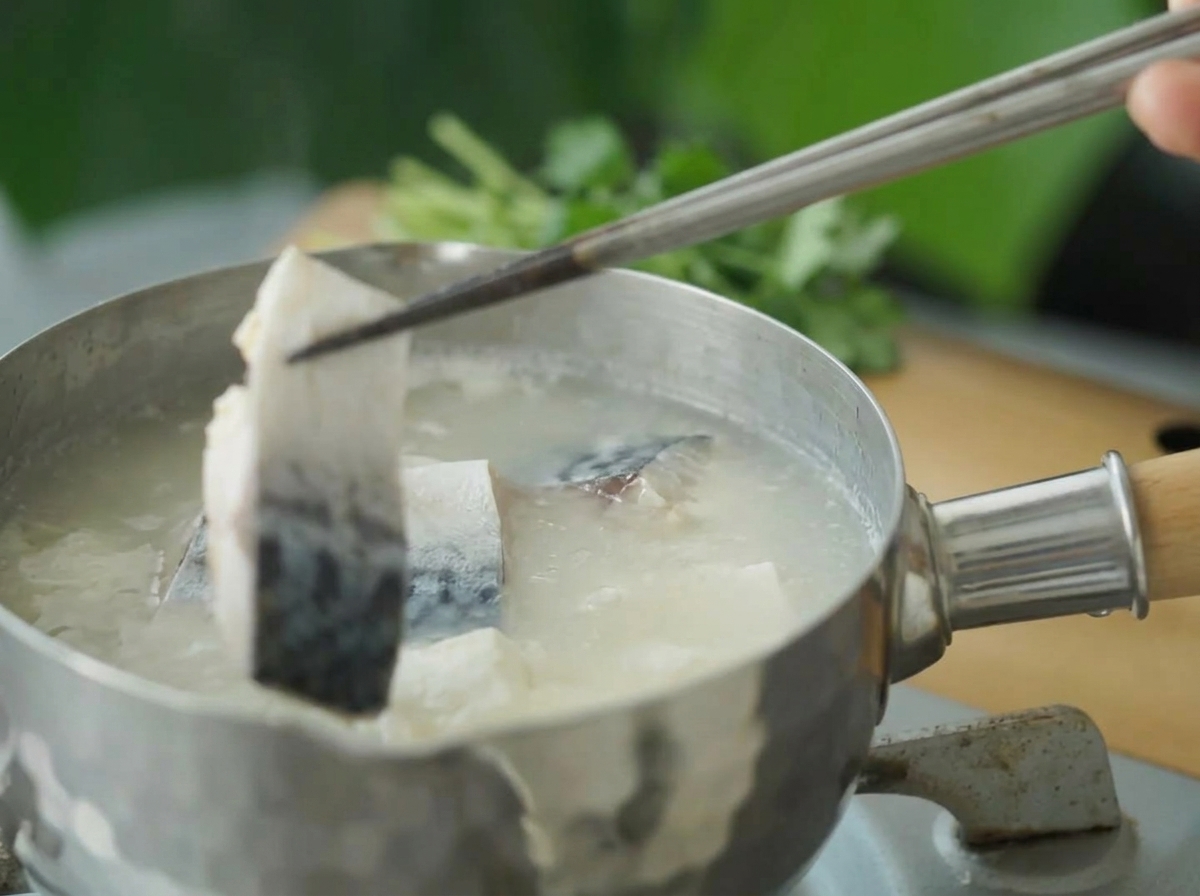 Stücke der blanchierten Makrele werden mit Essstäbchen in die kochende Suppe herabgelassen.