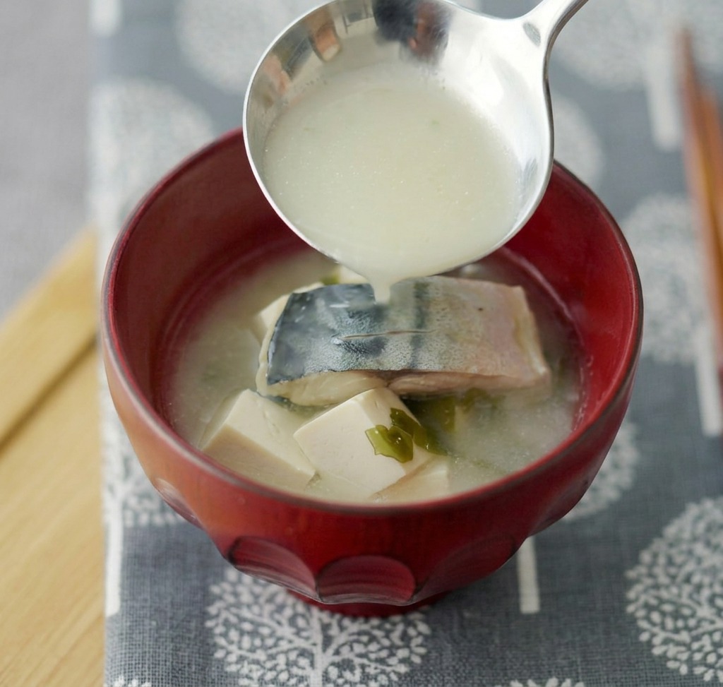 Miso-Suppe mit Makrele und Tofu wird in eine tiefrote Keramikschale geschöpft.