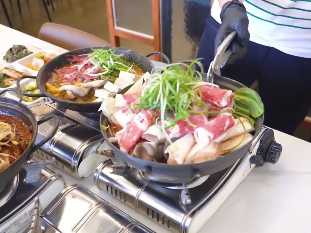 Eine gusseiserne Pfanne wird mit einer Schicht aus gekochtem Rettich und Kimchi am Boden vorbereitet.