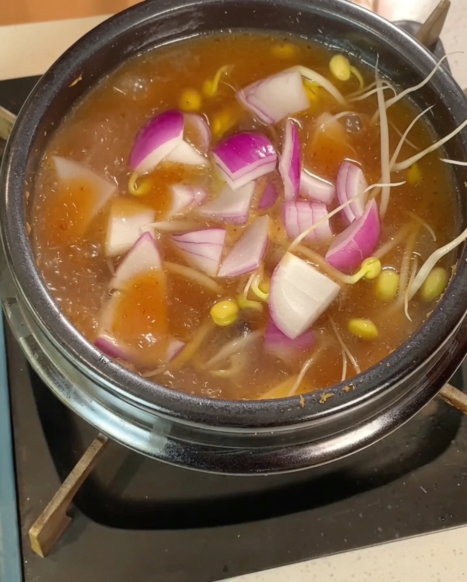 Sojasprossen, rote Zwiebelstreifen und Tofuwürfel garen im kochenden Eintopf.