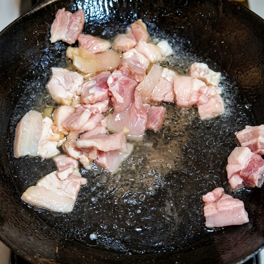 Goldbraune Schweinebauchwürfel braten in ausgelassenem Schmalz in einem traditionellen Wok.