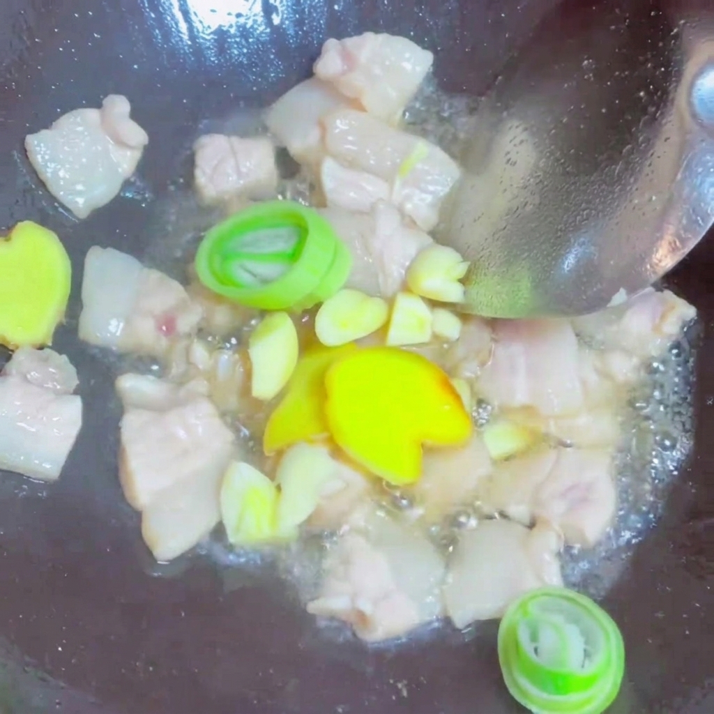 Scheiben von frischem Ingwer, Knoblauch und Frühlingszwiebelringe werden mit den gebratenen Fleischstücken im Wok geschwenkt.