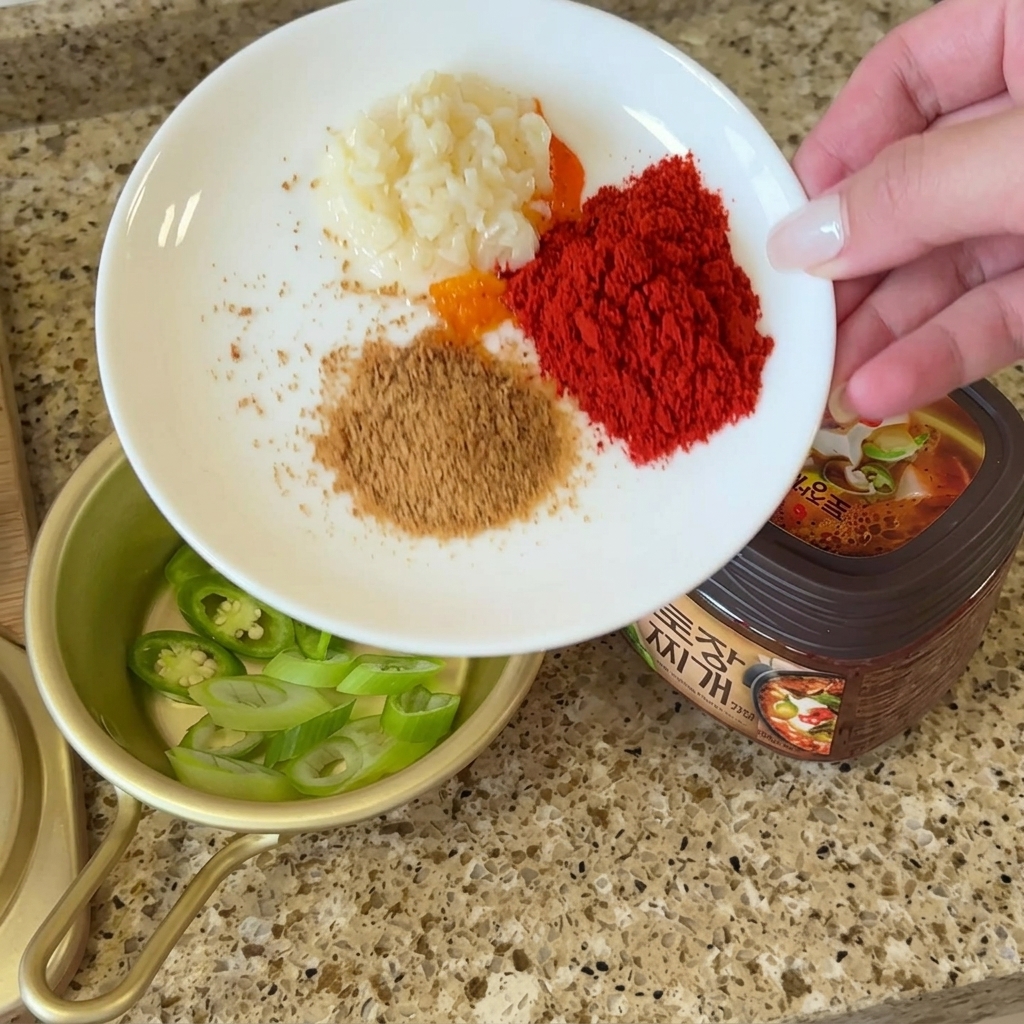 Ein weißer Teller mit gehacktem Knoblauch, Chilipulver, Rinderbrühe und Perilla-Pulver neben der Doenjang-Paste.