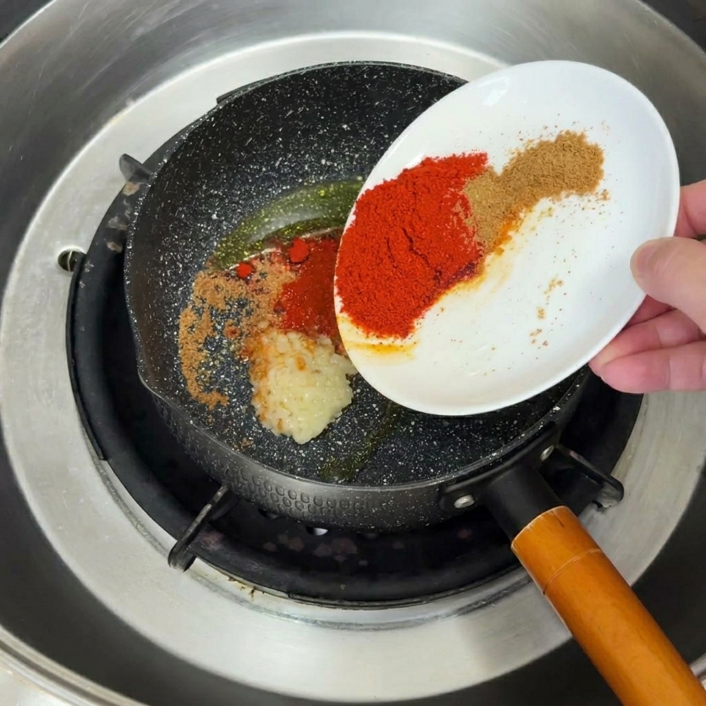 Gehackter Knoblauch und Gewürze brutzeln in heißem Öl in einer Pfanne.