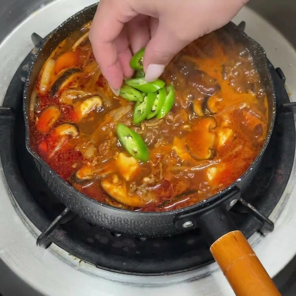 Ein heißer Topf Eintopf, garniert mit grünen Chilischeiben und frischen Frühlingszwiebeln.