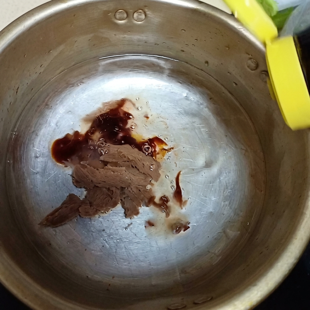 Austernsauce und ein Spritzer Fischsauce werden über der Sojabohnenpaste in den Metalltopf gegossen.