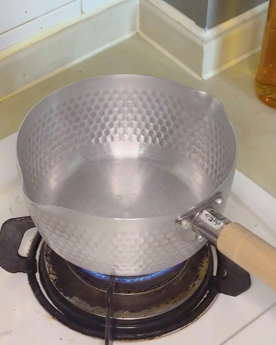 Klares Wasser wird in einen Metalltopf auf einem Gasherd gegossen.