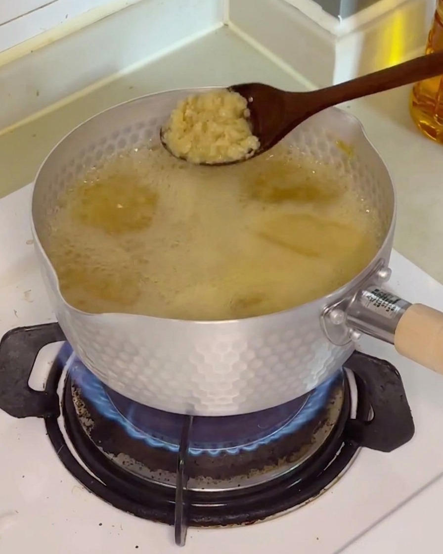 Ein Löffel frischer gehackter Knoblauch wird in die köchelnde, hellbraune Brühe gegeben.