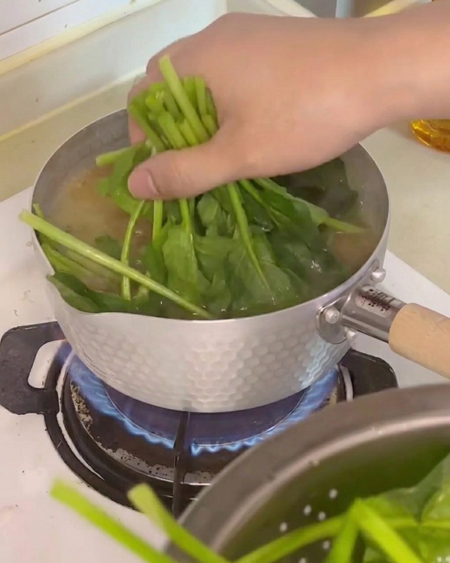 Spinat, Tofuwürfel und Enoki-Pilze werden in den Suppentopf gegeben.