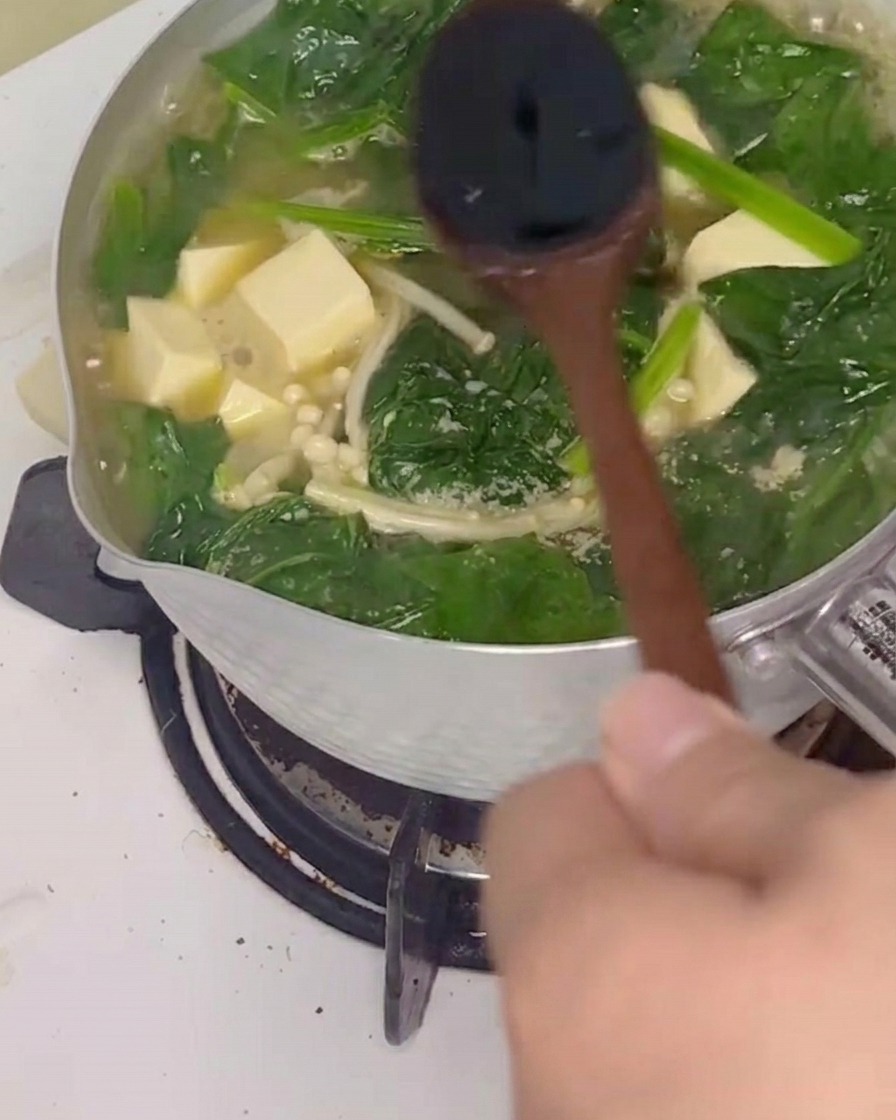Sojasauce wird mit einem Holzlöffel unter die Suppe gerührt.