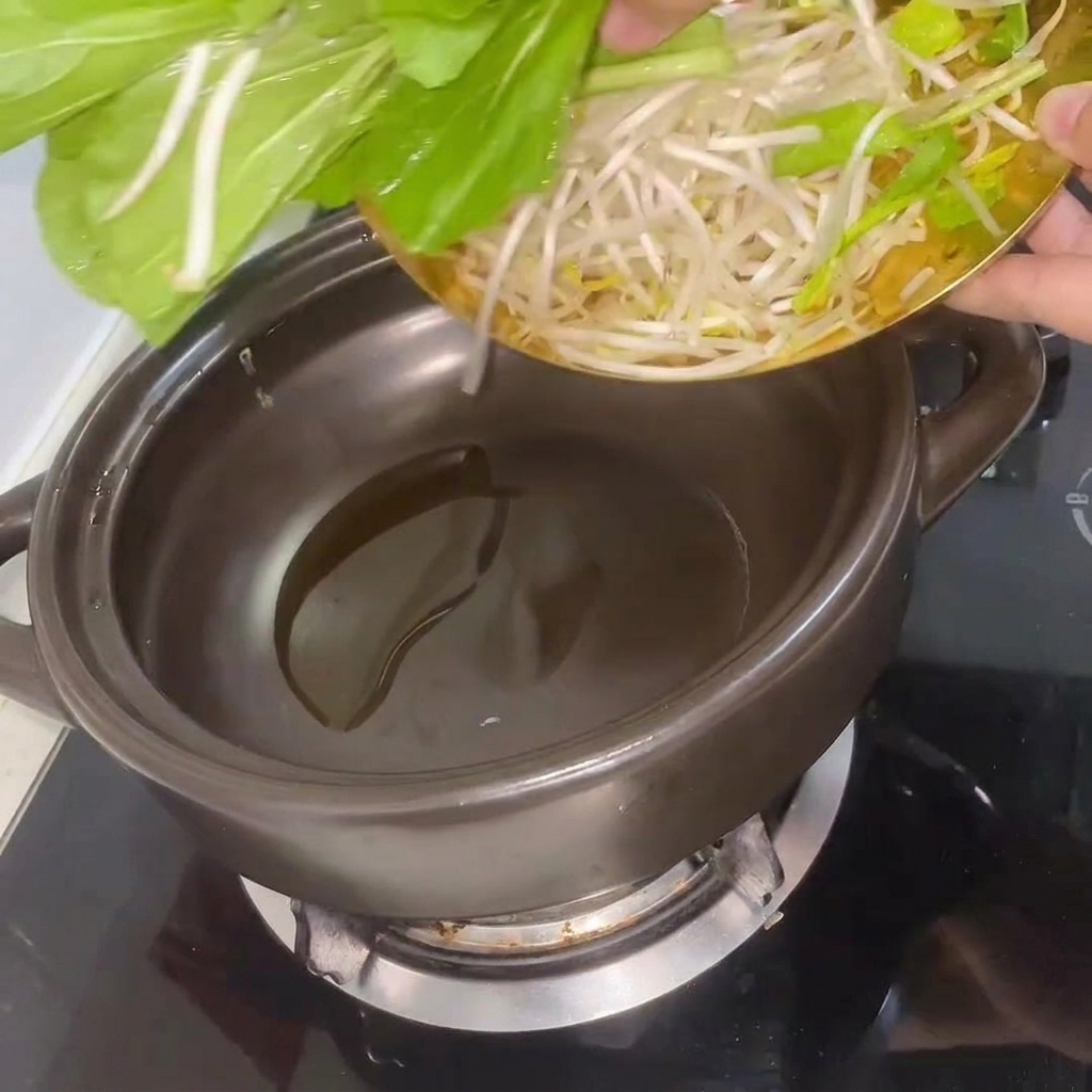 Frischer Bok Choy und Sojasprossen werden im erhitzten Tontopf umgerührt.