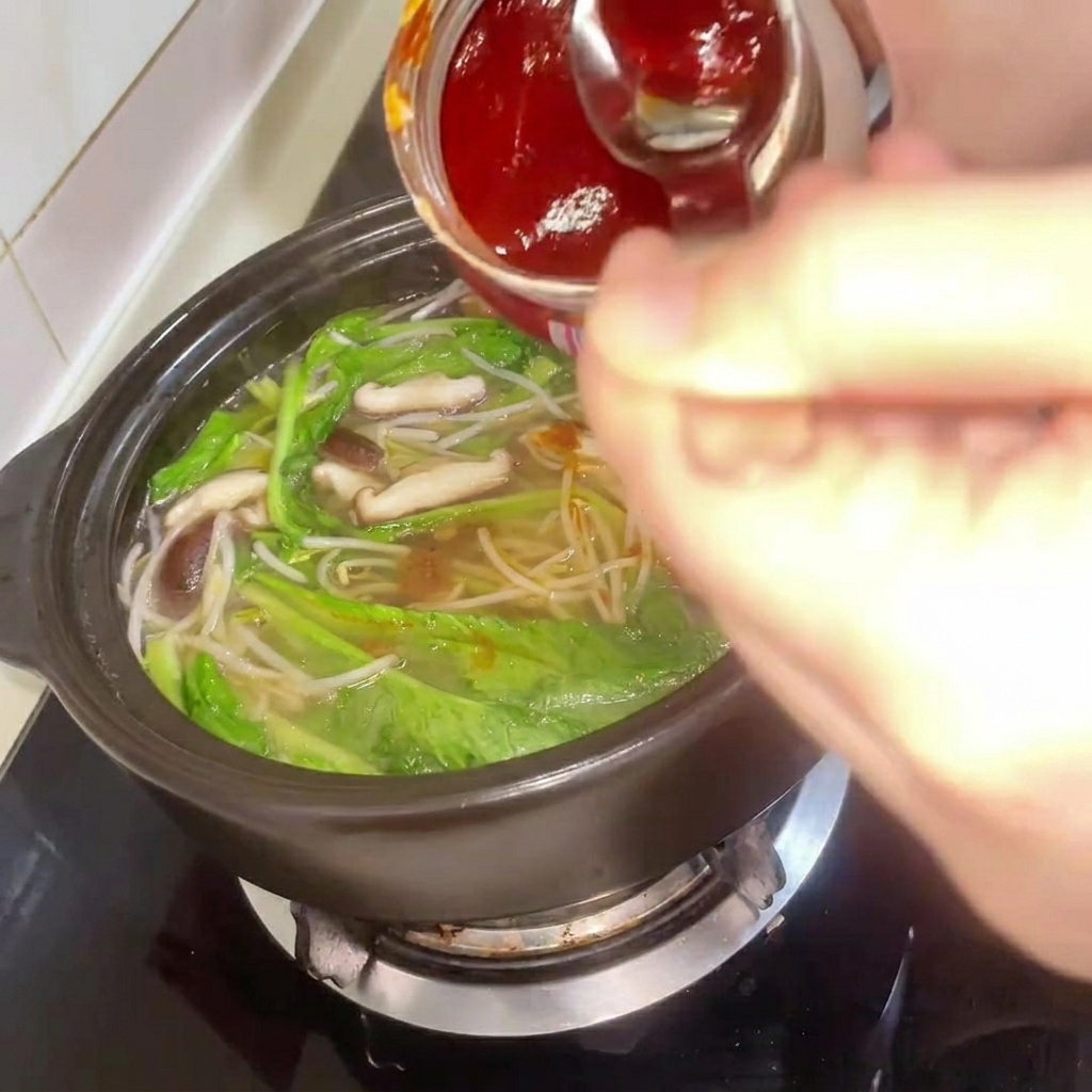 Koreanische Chilipaste wird hinzugefügt, während die Brühe umgerührt wird.