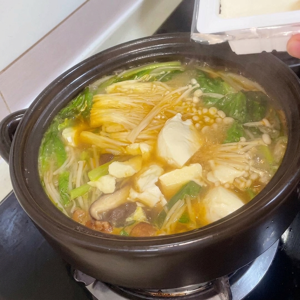 Frische Tofuwürfel werden vorsichtig in den köchelnden koreanischen Sojabohnen-Eintopf gelegt.