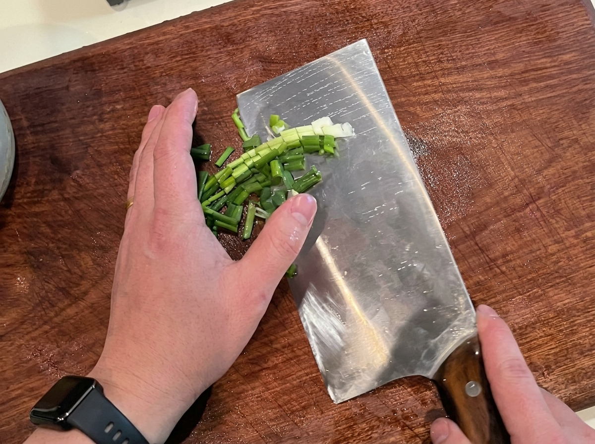 Frische grüne Frühlingszwiebeln werden auf einem Holzbrett in feine Ringe geschnitten.