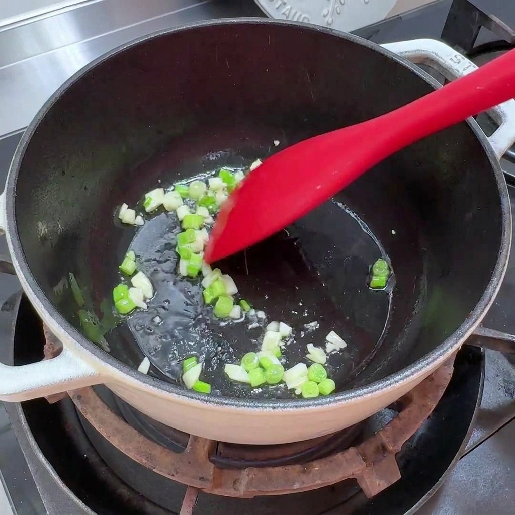 Gehackte Frühlingszwiebeln und gehackter Knoblauch brutzeln in etwas Öl in einem Topf.