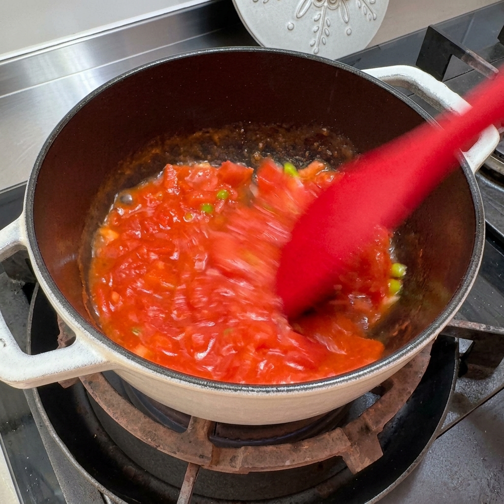 Tomaten werden im Topf zerdrückt und gerührt, um eine saucenartige Konsistenz zu erhalten.