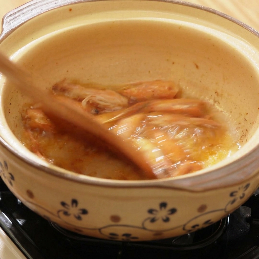 Heißes Wasser wird in einen Tontopf mit angebratenen Garnelenköpfen gegossen.
