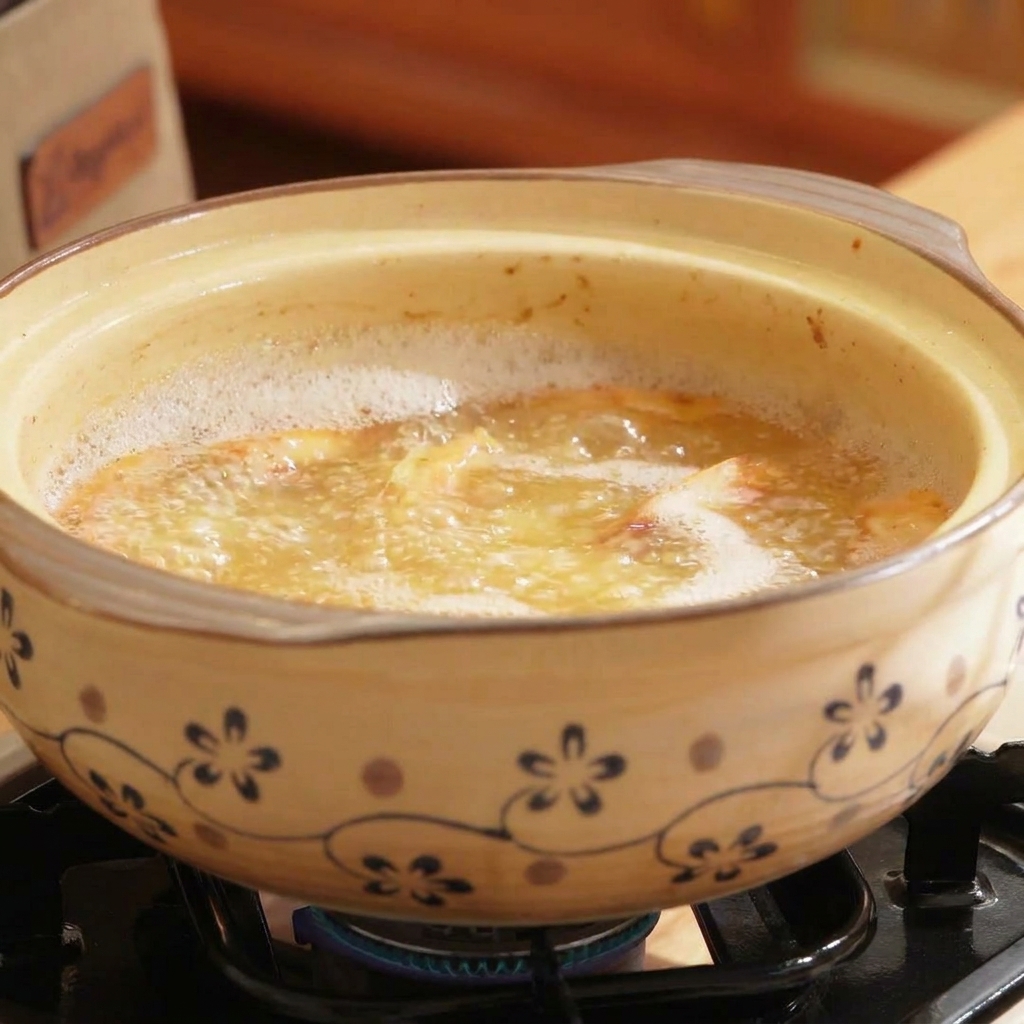 Ein Tontopf gefüllt mit kochender, orangefarbener Brühe, in die Meeresfrüchte- und Shiitake-Pilze gerührt werden.
