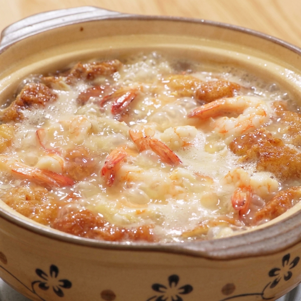 Ein dampfender Tontopf mit Suppe aus Garnelen, Tofu und Eiern, die mit weißem Pfeffer und Salz gewürzt wird.