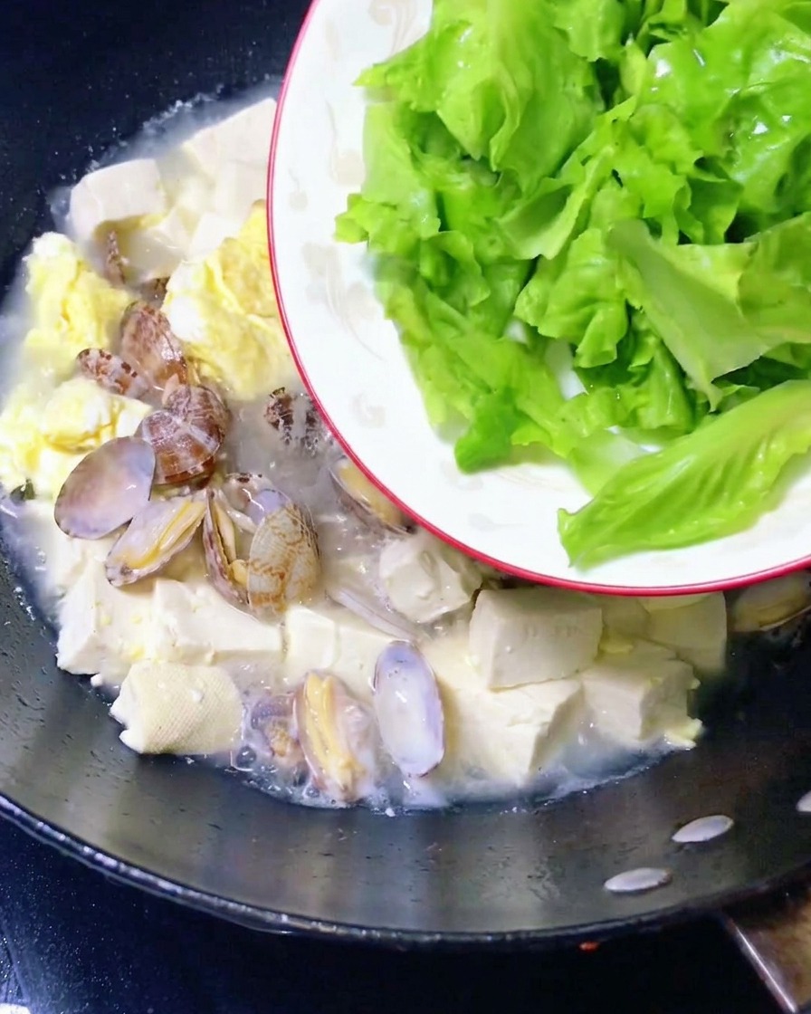 Frische Salatblätter werden in den fertigen Muscheleintopf gegeben.