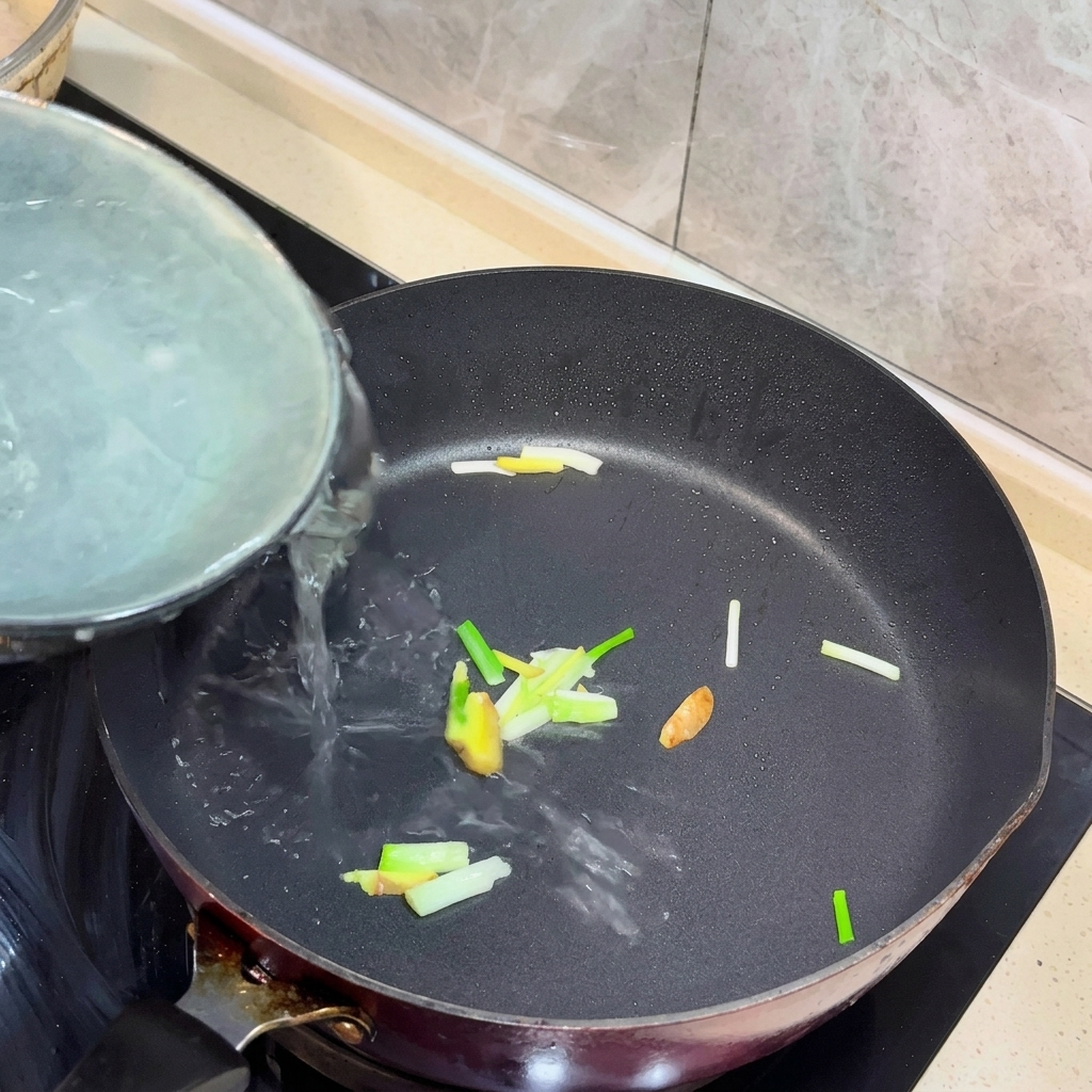 Kochendes Wasser wird in eine Pfanne mit angebratenem Ingwer und Frühlingszwiebeln gegossen.