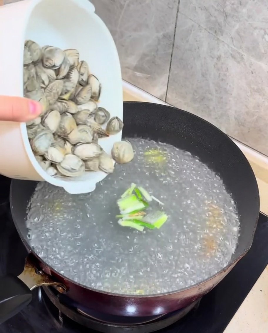 Frische Muscheln und gewürfelter Tofu werden in die kochende Brühe gegeben.