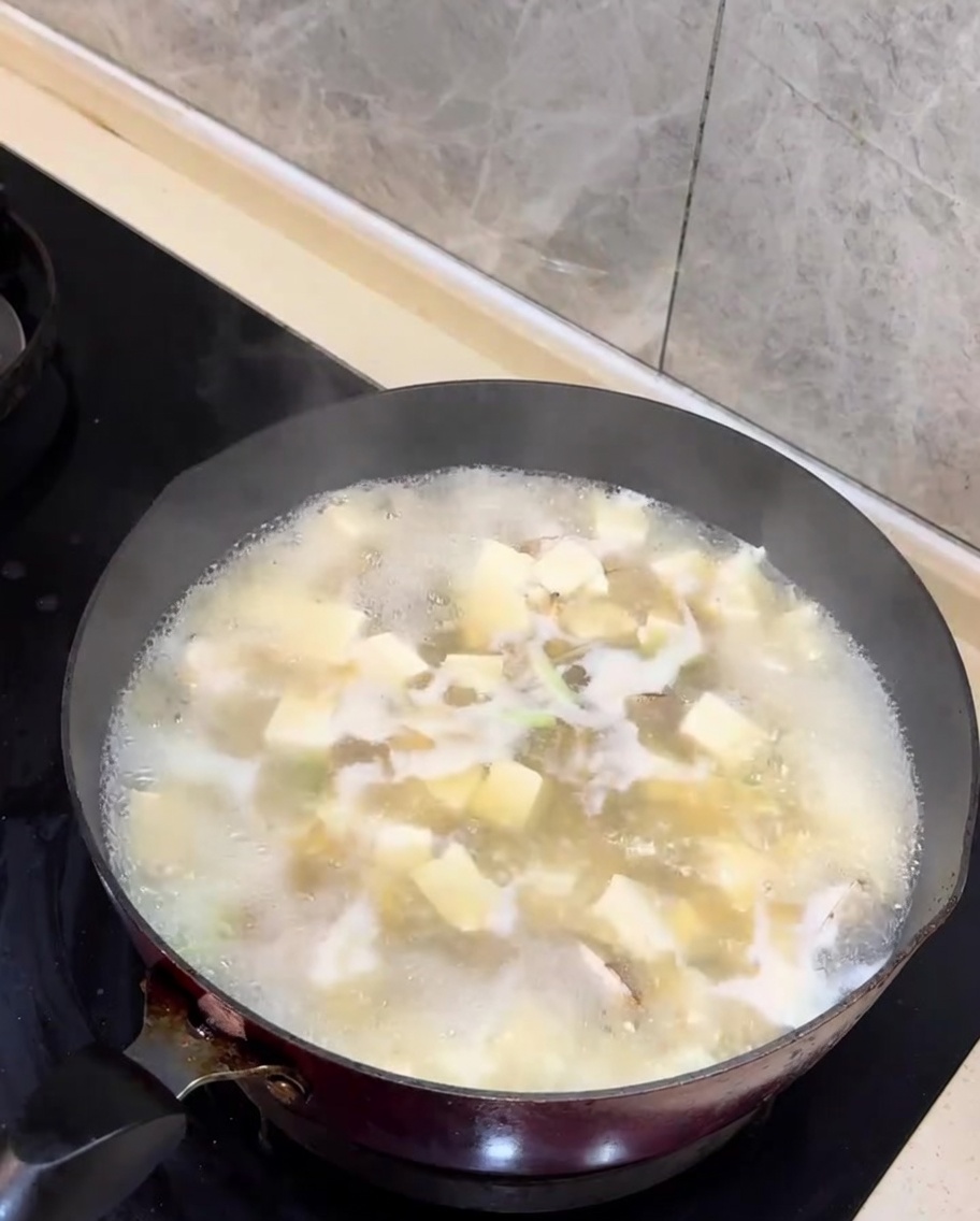 Gehacktes Frühlingszwiebelgrün wird zur fertigen Muschel-Tofu-Suppe gegeben.