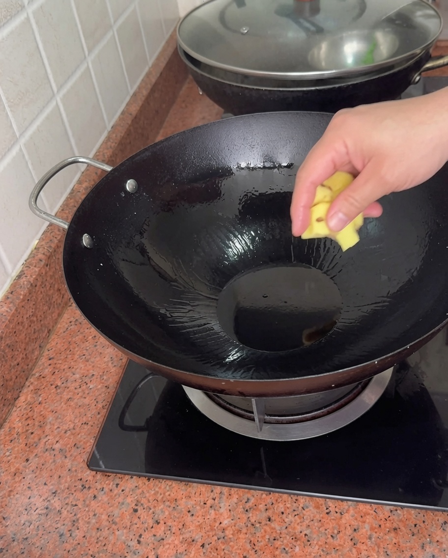 Eine Hand legt ein Stück Ingwer in einen heißen Wok mit Öl.