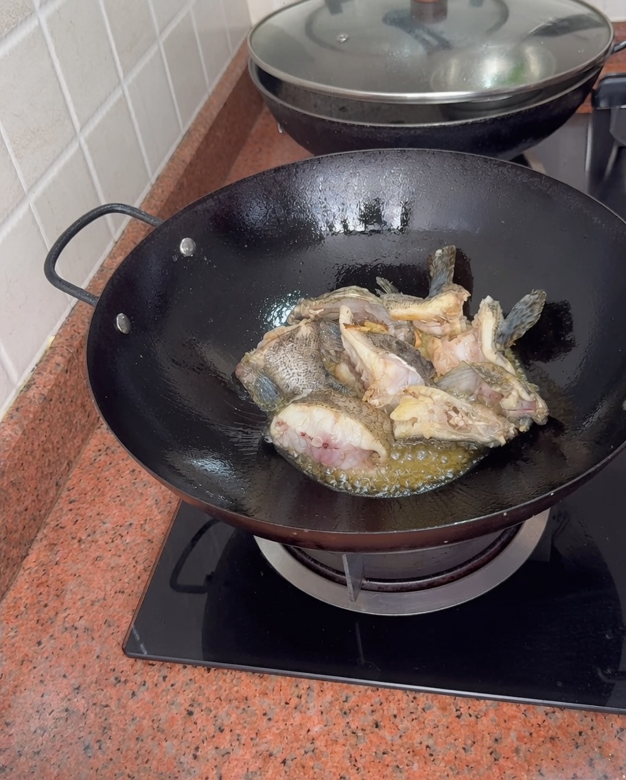 Zackenbarschstücke köcheln im Wok, während kochendes Wasser hinzugefügt wird, was eine dicke, weiße Fischbrühe erzeugt.