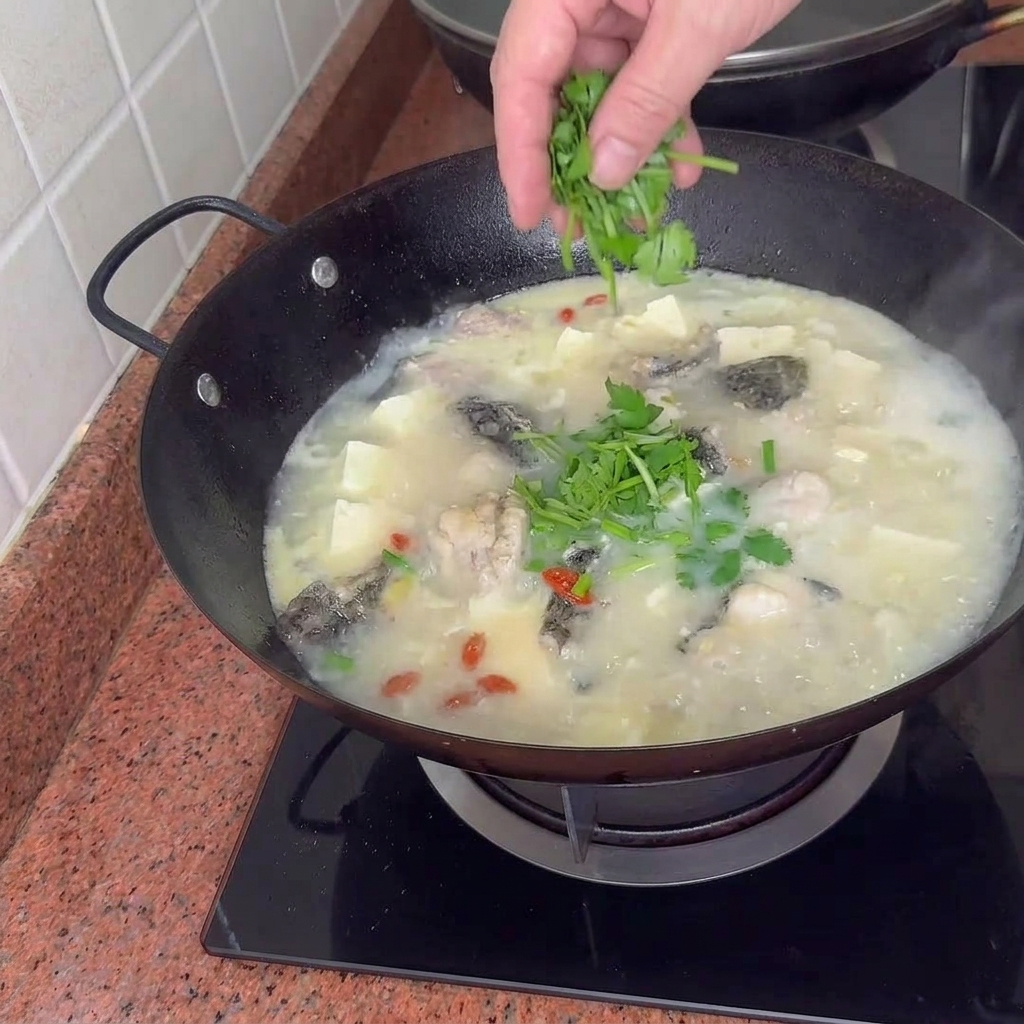 Ein fertiger Topf mit cremiger Fisch-, Tofu- und Muschelsuppe, garniert mit leuchtend grünen Frühlingszwiebeln.