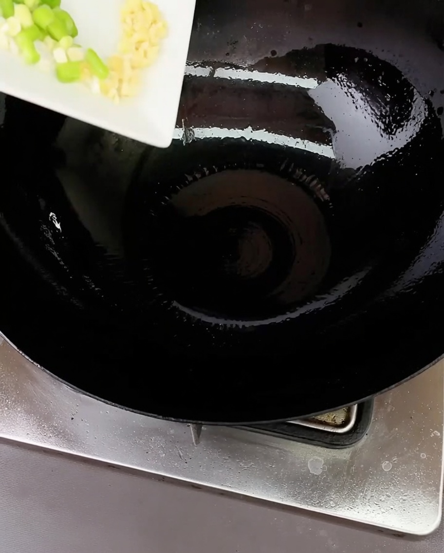Gehackte Frühlingszwiebeln und Knoblauch braten in einem Wok mit wenig Öl an.