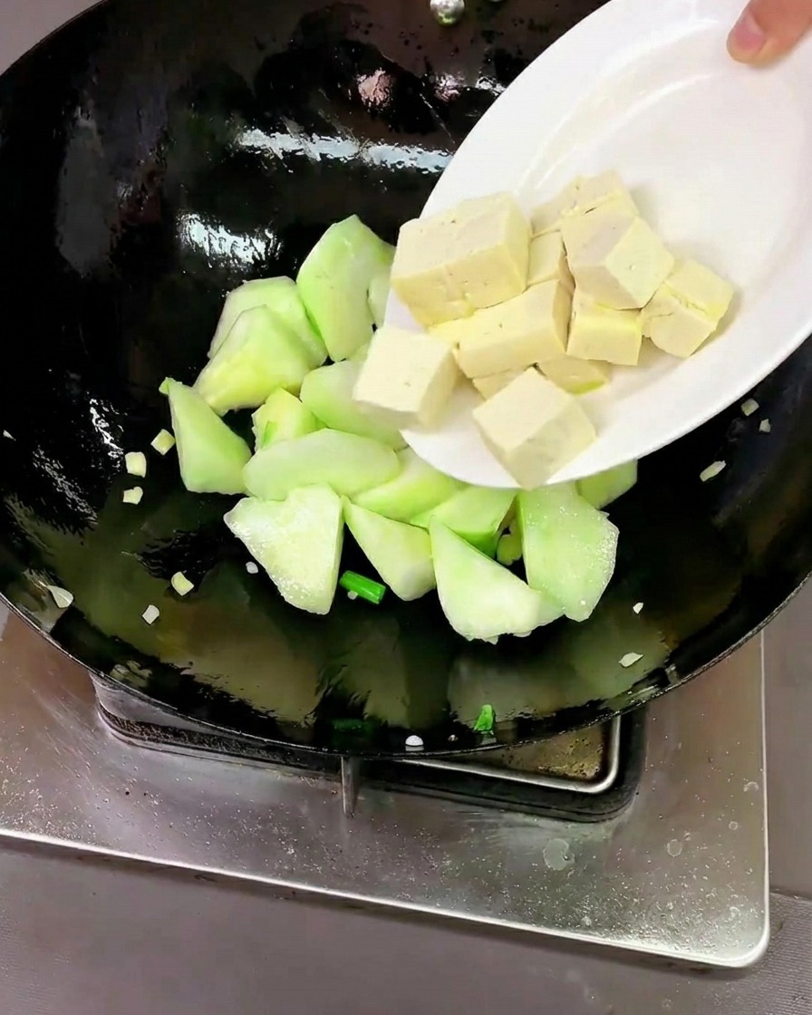 Tofu-Würfel und rohe Muscheln werden in den Wok zur Luffa gegeben.