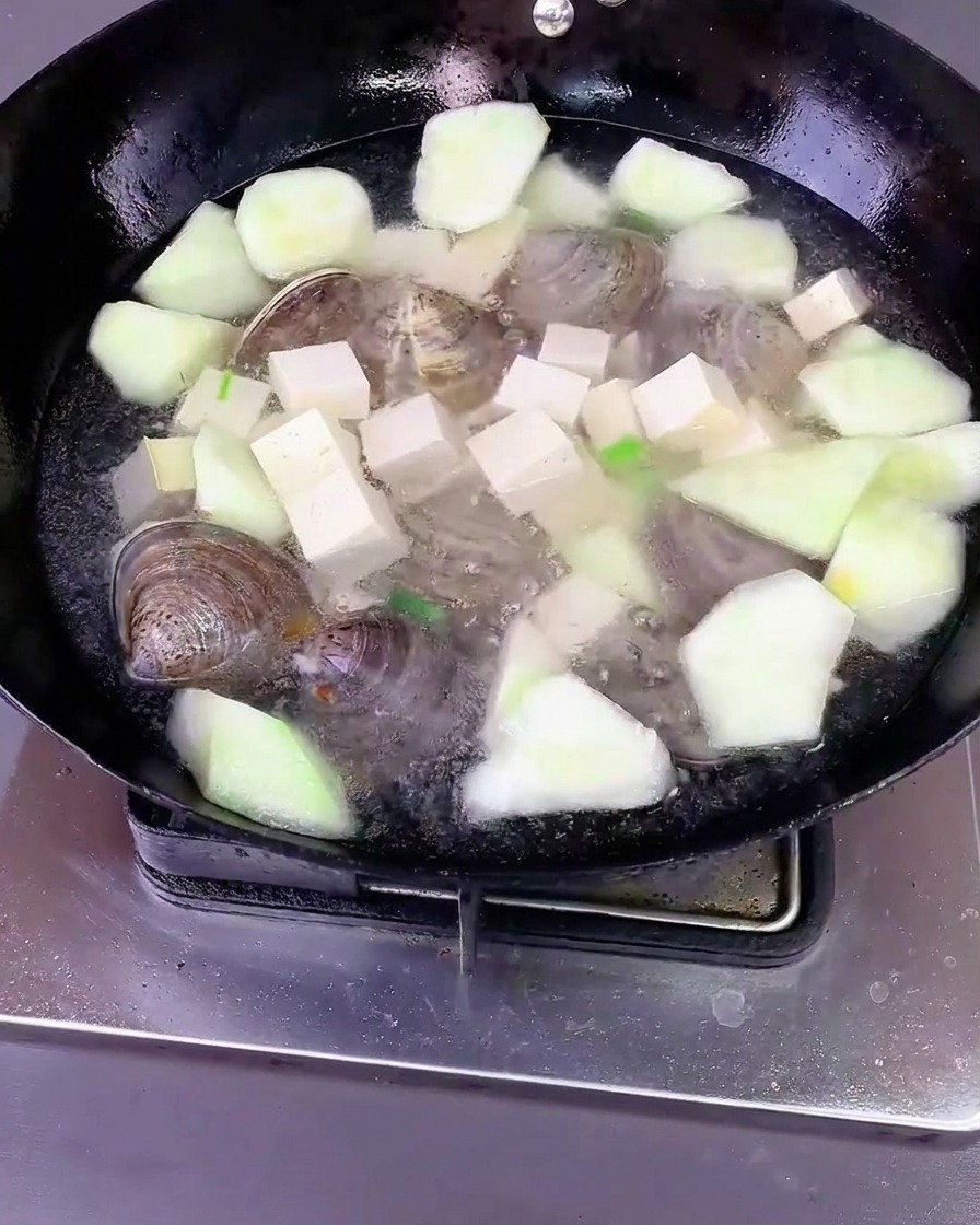 Wasser wird über Luffa, Tofu und Muscheln in einen Wok gegossen, dann wird mit einem Deckel abgedeckt.