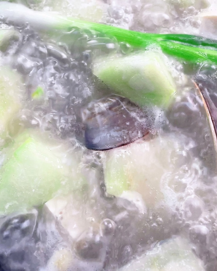 Mit einer Kelle wird Schaum von der Oberfläche der kochenden Suppe entfernt.