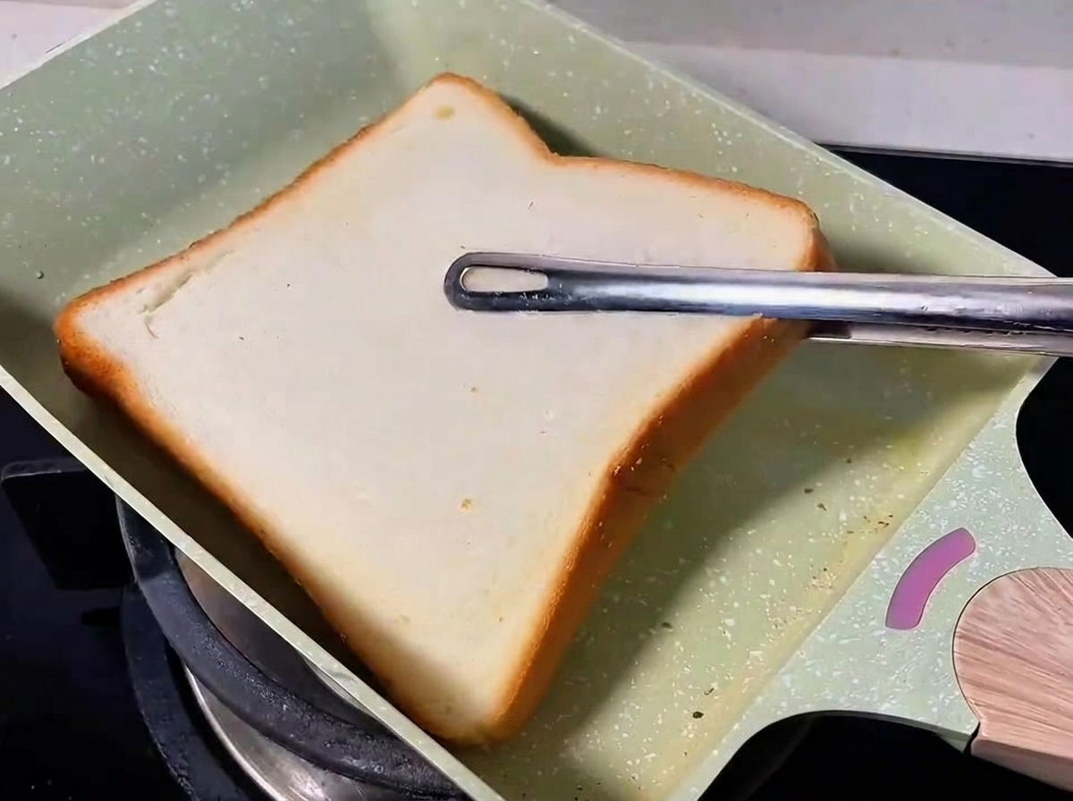 Eine Brotscheibe wird in einer grünen Pfanne getoastet.