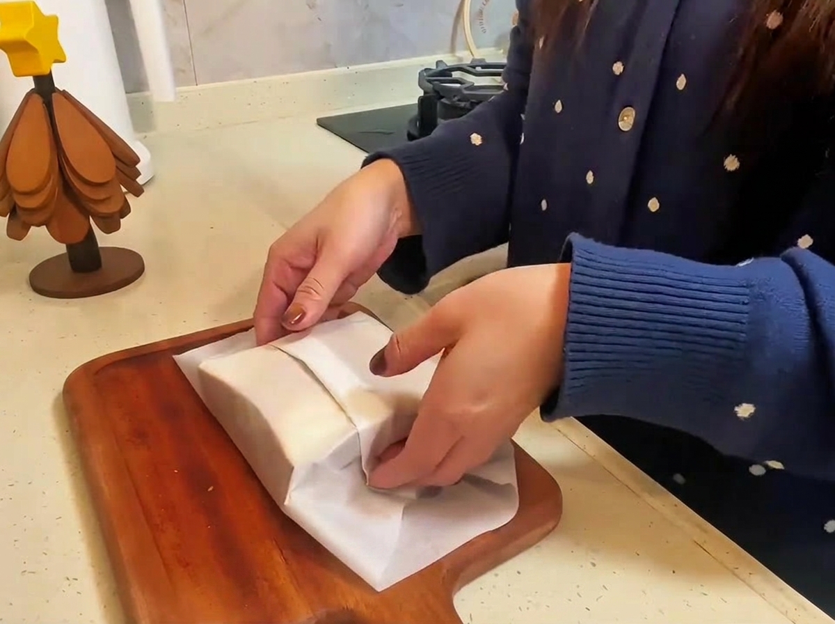 Das fertige Sandwich in Backpapier eingewickelt und auf einem Brett halbiert.