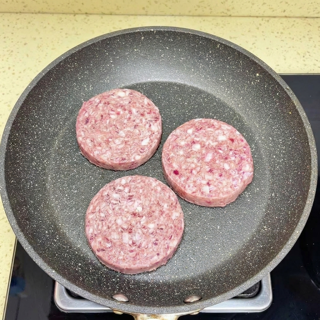 Rinderhackfleisch wird in einer heißen Pfanne mit einem weißen Pfannenwender krümelig zerkleinert.