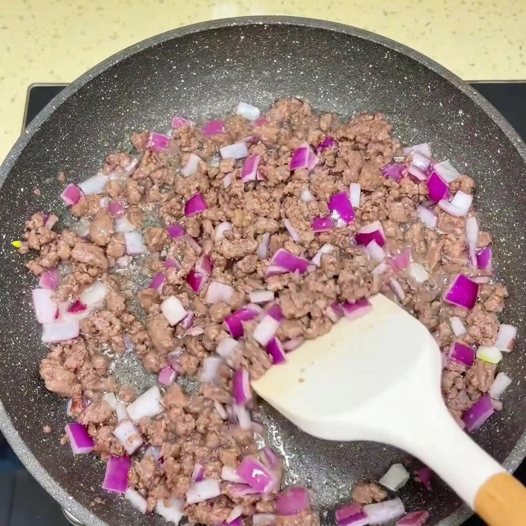 Angebratenes Rinderhackfleisch und gehackte rote Zwiebeln werden in der Pfanne mit Soßen gewürzt.
