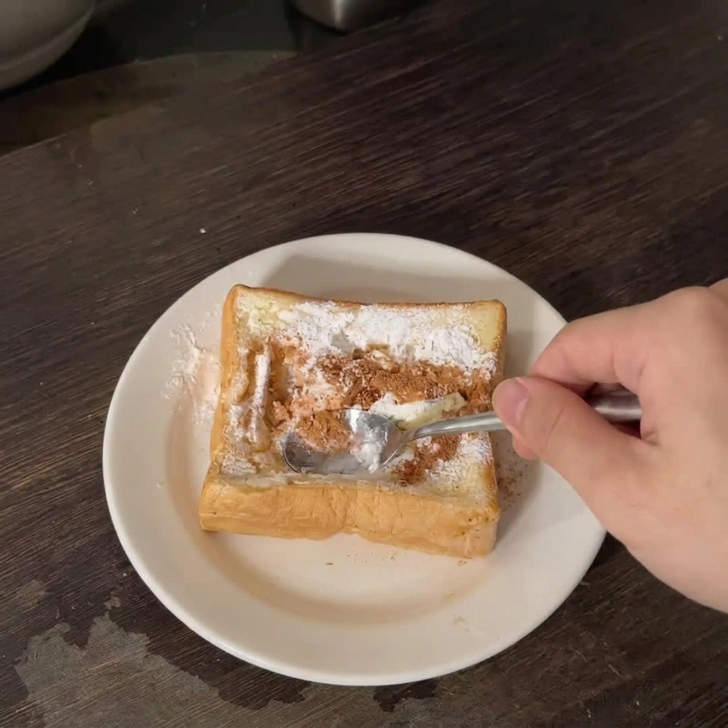 Eine Hand drückt mit einem Metalllöffel die Mitte einer dicken Scheibe Toastbrot ein.