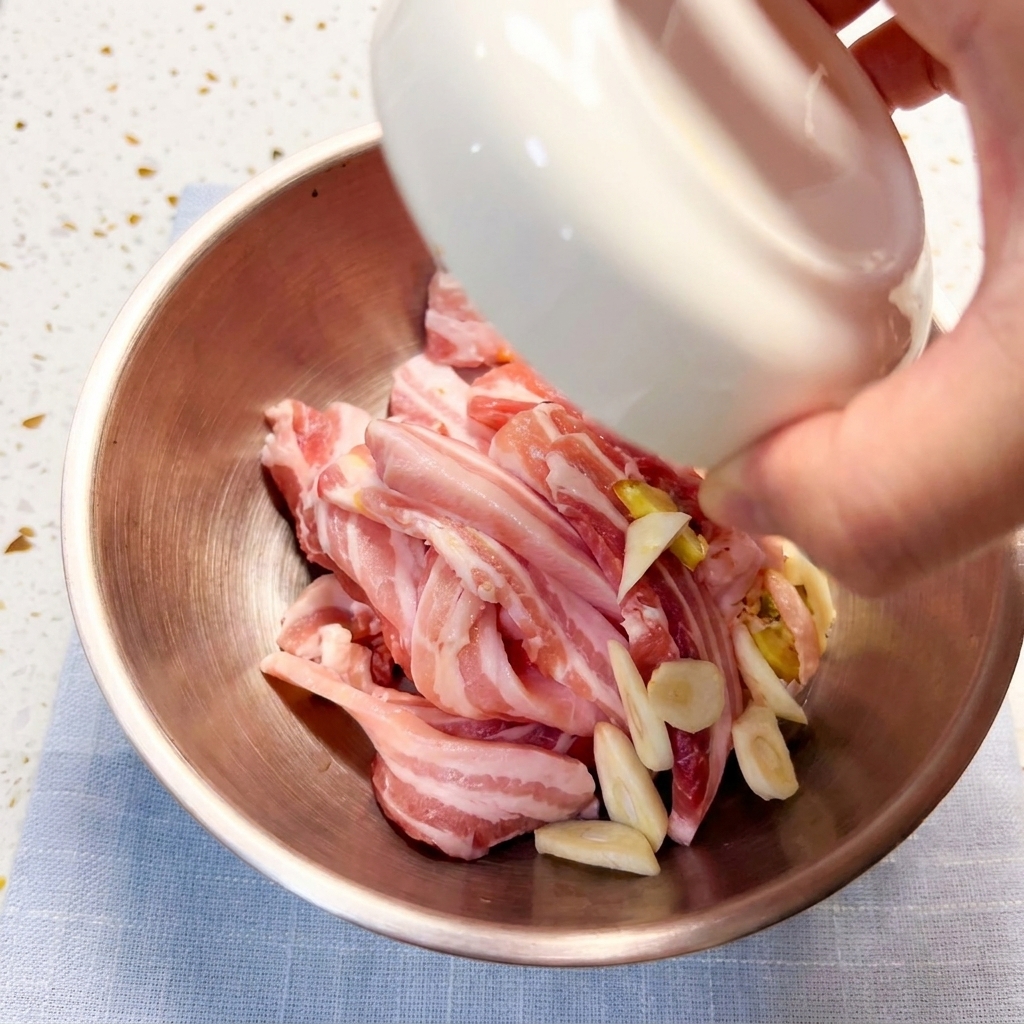 Schweinebauchstreifen werden in einer Metallschüssel mit Gewürzen mariniert.