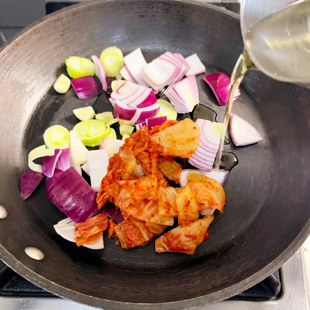 In einer Pfanne werden rote Zwiebeln, Frühlingszwiebeln und Kimchi in Öl angebraten.
