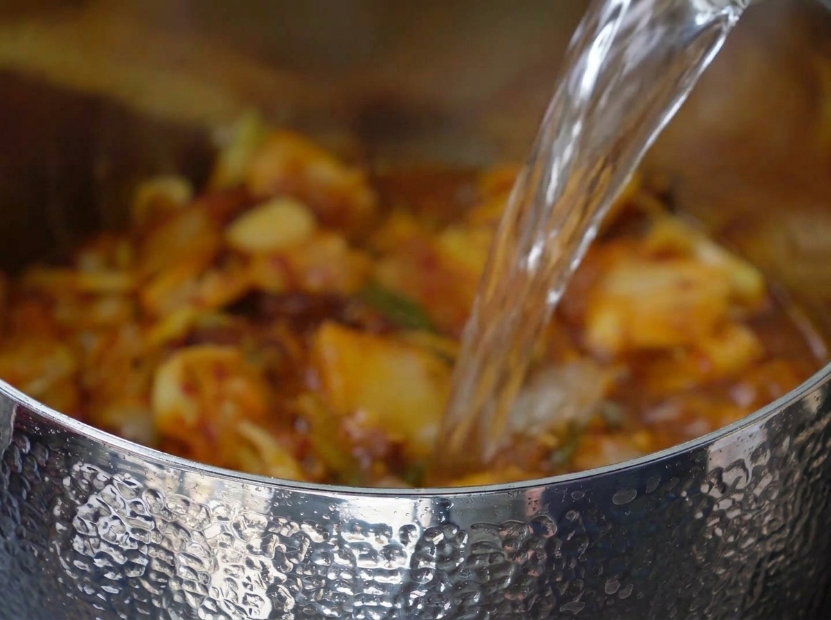 Wasser wird in den Topf zu der Kimchi-Schweinefleisch-Mischung gegossen.