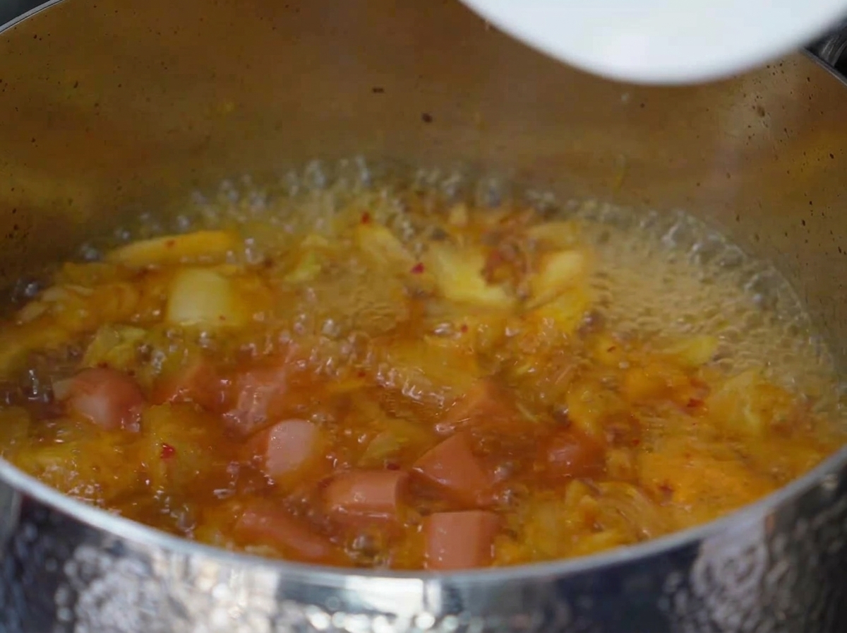 Scheiben von Spam und Wurst köcheln in der sprudelnden, gewürzten Kimchi-Brühe.