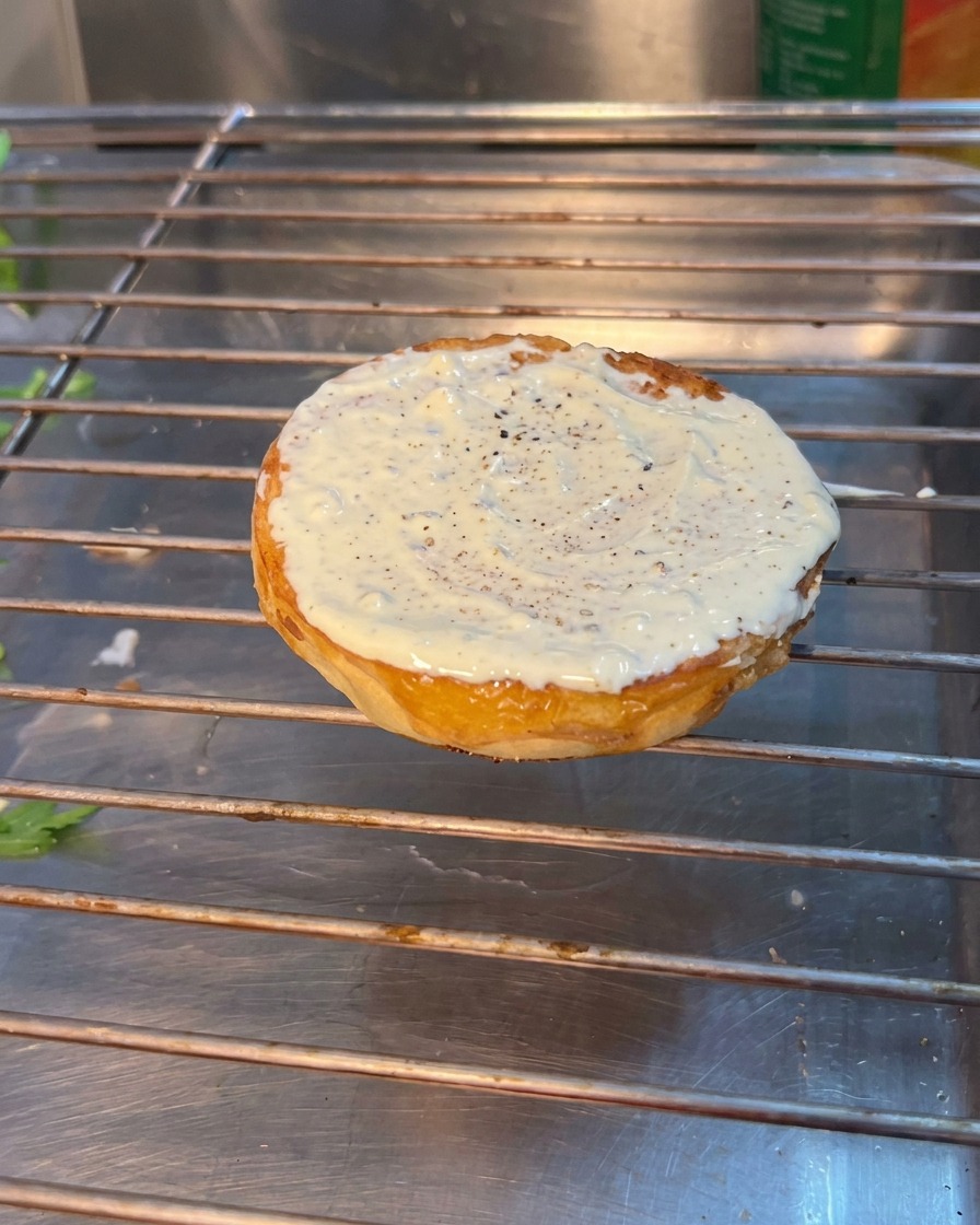 Ein Burger-Zusammenbau zeigt Rucola, Tomate und Gewürzgurken, die auf das untere getoastete Brötchen geschichtet werden.