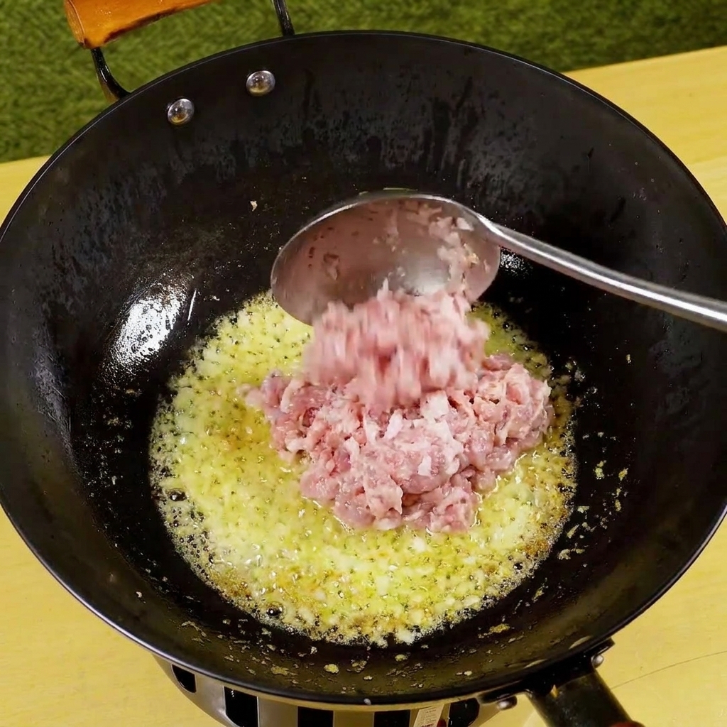 Hackfleisch wird in die Pfanne mit Zwiebeln und Knoblauch gegeben und beginnt zu bräunen.