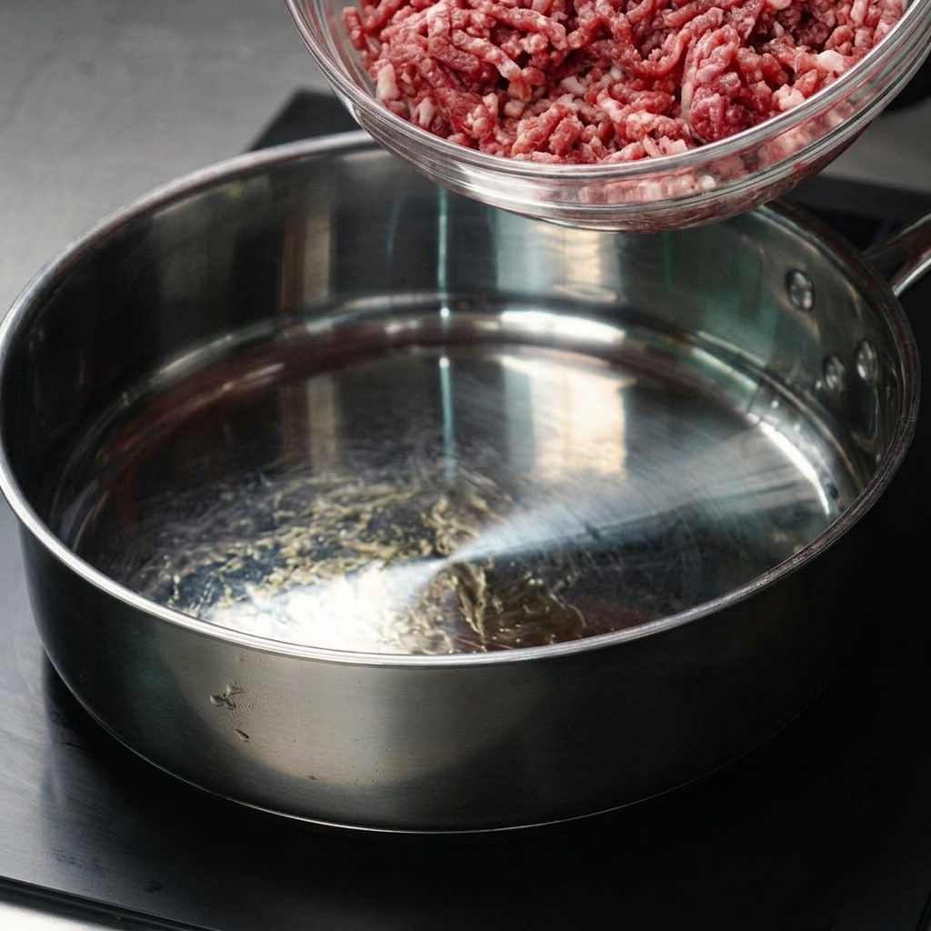 Rinderhackfleisch wird aus einer Glasschüssel in eine heiße Bratpfanne gegeben.