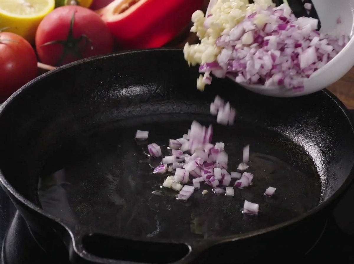 Gewürfelte Zwiebeln und gehackter Knoblauch werden in eine heiße, geölte Gusseisenpfanne gegeben.