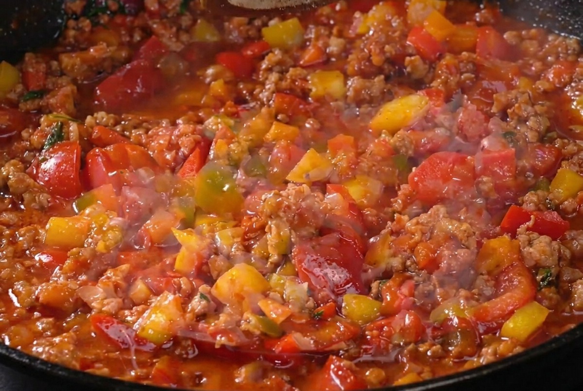 Die Fleischsauce köchelt in der Pfanne und wird mit Pfeffer gewürzt. Sie zeigt eine sämige, dicke Konsistenz.